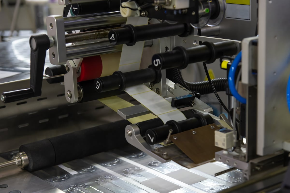 A printing machine is actively running, applying labels onto a roll of material within a manufacturing facility