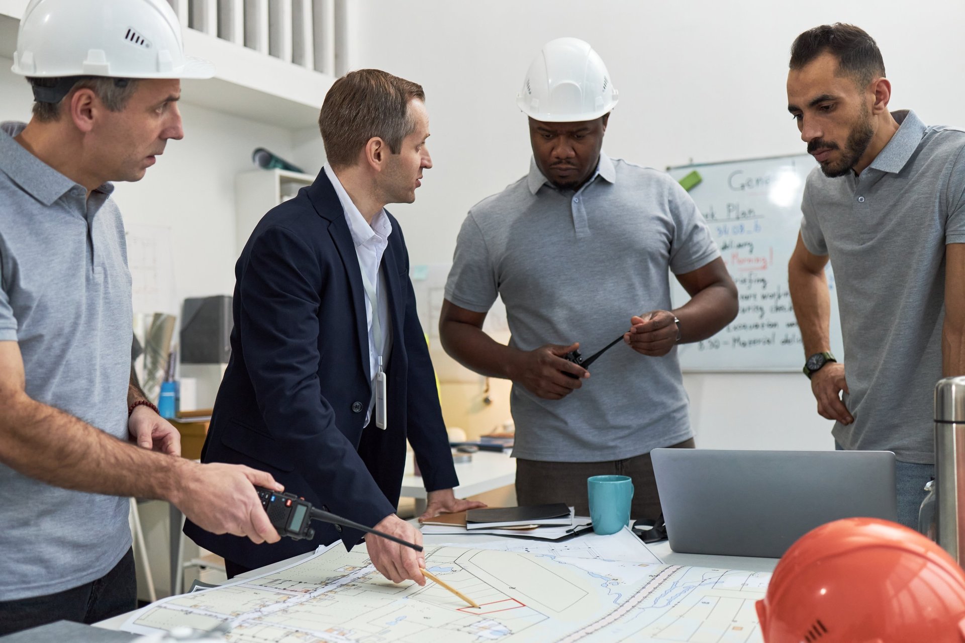 Middle aged man in suit discussing construction plans with engineers around table with blueprints