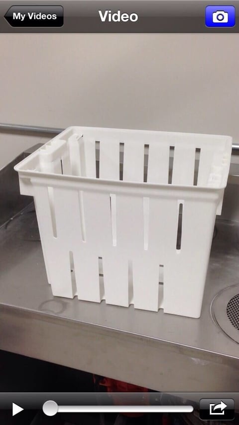 White plastic drain basket with vertical slots sitting on a metal kitchen counter
