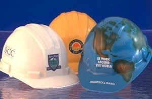 Three hard hats in white, orange, and blue with company logos displayed on a wooden surface against a dark blue background