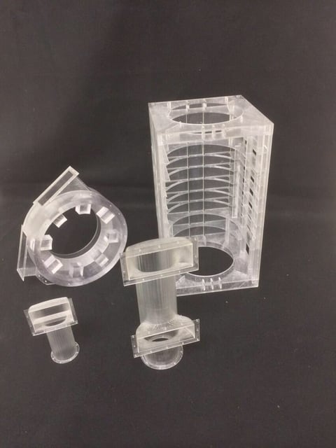 Disassembled clear plastic cylindrical filters and housing components displayed against dark background